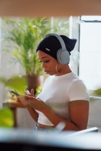 A woman with headphones listening to Scale Your Joy podcast by Kaneisha Grayson and browsing her smartphone.